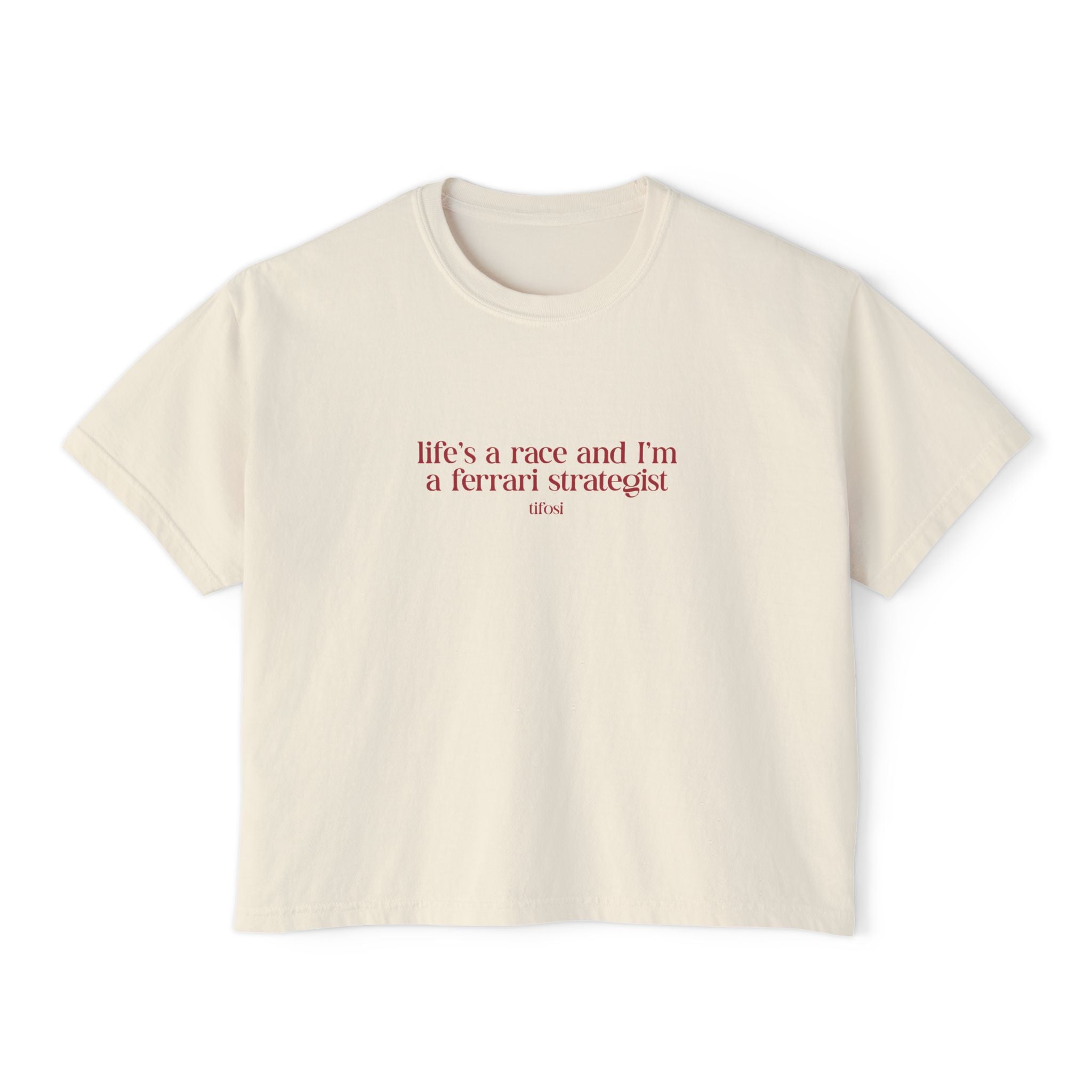 An off-white short-sleeve crewneck t-shirt with a red printed quote on the chest reading 'life's a race and I'm a ferrari strategist' and 'FERRARI' underneath, displayed on a clean white background.