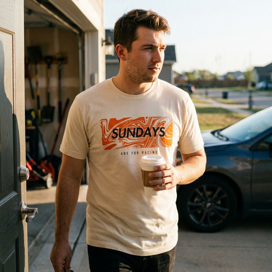 Man wearing a 'Sundays are for racing' t-shirt holding a coffee cup, standing in front of a garage.