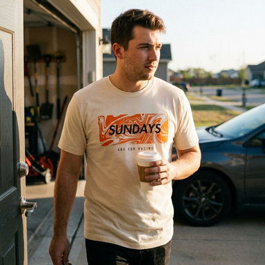 Man wearing a 'Sundays are for racing' t-shirt holding a coffee cup, standing in front of a garage.
